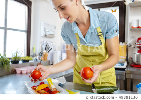 Smiling woman in kitchen holding tomatoes Smiling woman in kitchen holding tomatoes 49881130