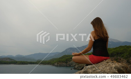 Female tourist sitting on a rock on clear sky and calm sea background 49883462