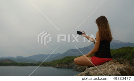 Female tourist sitting on a rock on clear sky and calm sea background 49883477
