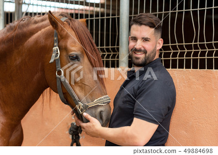 Portrait of a handsome man with his horse standing at the stable