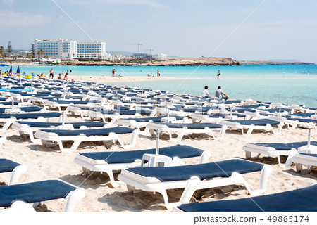 Umbrellas and chaise lounges on the beach. Plastic sunbeds near the sea. Tropical vacation, summer 49885174