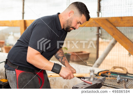 Blacksmith working on the anvil, making a horseshoe. Blacksmith working on the anvil, making a horseshoe. 49886584