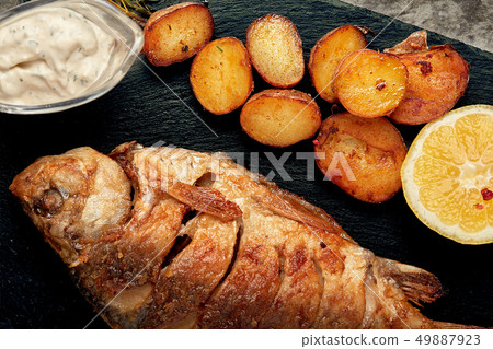 Grilled whole fish Served with baked potatoes, lemon and sauce. Top view. Grilled whole fish Served with baked potatoes, lemon and sauce. Top view. 49887923