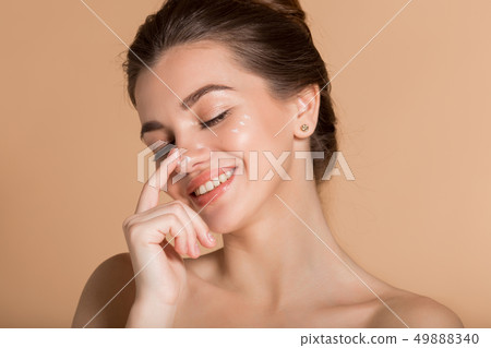 Happy smiling girl with perfect skin with moisturizing face cream on a cheek. Skin care and health Happy smiling girl with perfect skin with moisturizing face cream on a cheek. Skin care and health 49888340