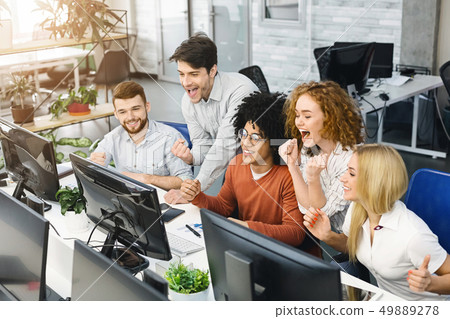 Cheerful emotional team reading winning results on monitor Cheerful emotional team reading winning results on monitor 49889278