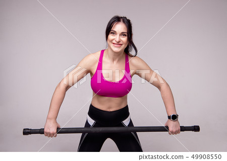 Beautiful muscular woman doing exercise with gymnastic stick on a gray background. 49908550