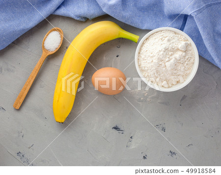 The ingredients for the banana cake on gray background. Wooden Spoon, Banana, Eggs The ingredients for the banana cake on gray background. Wooden Spoon, Banana, Eggs 49918584