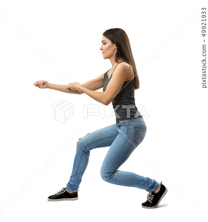 Side view of young woman in sleeveless gray top and blue jeans doing kata with long step right Side view of young woman in sleeveless gray top and blue jeans doing kata with long step right 49921933