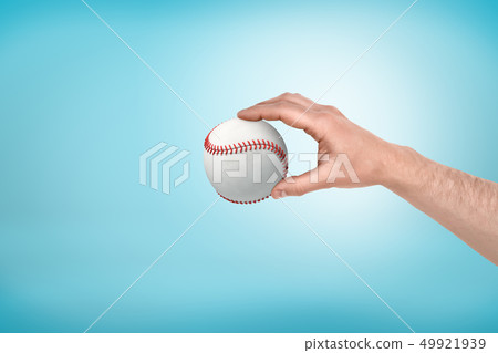 Side view of man's hand holding white baseball on light-blue background with some copy space. 49921939