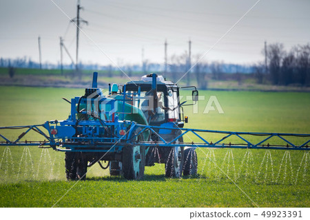 Blue tractor with spraying device in green field Blue tractor with spraying device in green field 49923391