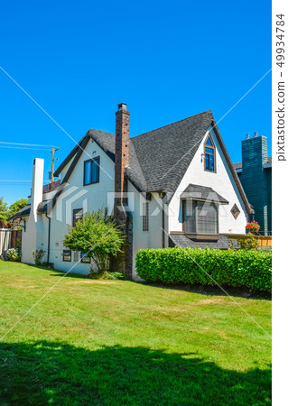 Old style family house with lawn and hedgerow in front on blue sky background 49934784