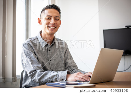 坐在膝上型計算機前面的微笑的人 坐在膝上型計算機前面的微笑的人 49935198