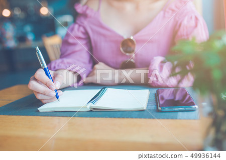 The woman's hand is writing on a notebook. The woman's hand is writing on a notebook. 49936144