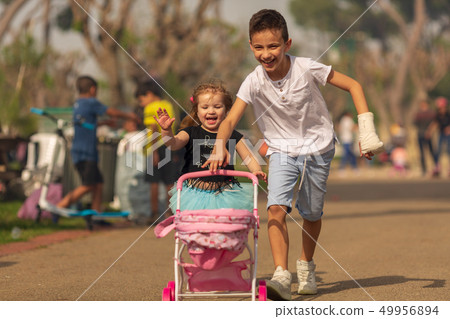 boy and girl play a game of children playing in a pram in a park. Children's friendship. Children 49956894