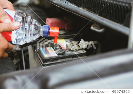 mechanic pouring distilled water to fill car battery in automobile repair service mechanic pouring distilled water to fill car battery in automobile repair service 49974263