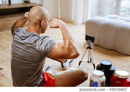 Bodybuilder wearing grey t-shirt and red shorts showing biceps Bodybuilder wearing grey t-shirt and red shorts showing biceps 49976667