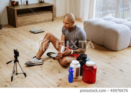Sportsman sitting on floor and making blog about supplements 49976676