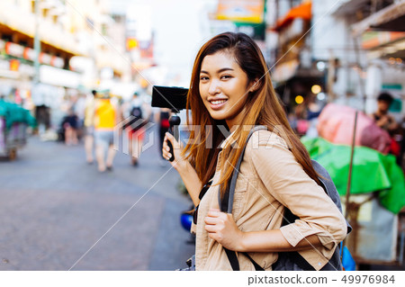 Young female tourist holding a gimbal with smartphone and recording videos 49976984