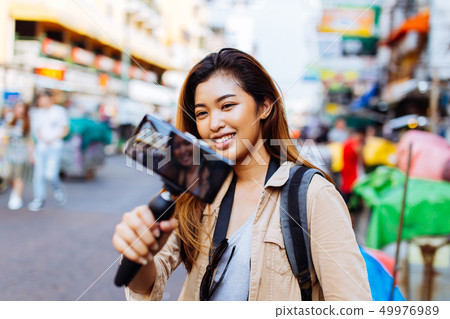 Young female tourist holding a gimbal with smartphone and recording videos 49976989