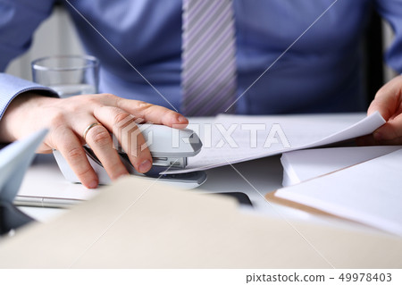 Male clerk arm pin together some papers with stapler 49978403