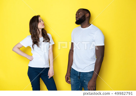 Unhappy interracial couple in white T-shirts posing for camera in studio Unhappy interracial couple in white T-shirts posing for camera in studio 49982791