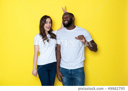 Smiling interracial couple in white T-shirts looking at camera in studio 49982795