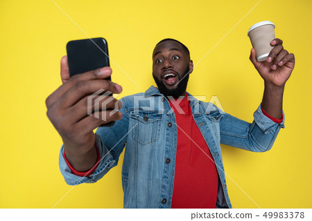 Waist up of funny African man keeping cupholder and smartphone in arms Waist up of funny African man keeping cupholder and smartphone in arms 49983378
