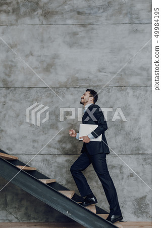 Cheerful man with gadget is walking upstairs 49984195
