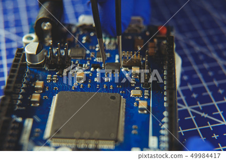 Microcircuit with tweezers on the background of electronic components 49984417
