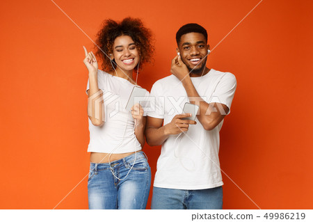 Positive african-american couple listening to music in headphones Positive african-american couple listening to music in headphones 49986219