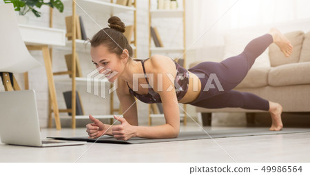 Fitness girl training yoga, watching online videos on laptop 49986564