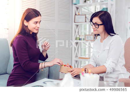 Dark-haired alluring pleasant psychologist offering candies to a young patient Dark-haired alluring pleasant psychologist offering candies to a young patient 49986565