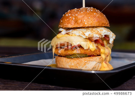 Close up tall tasty burger with cheese and egg served on tray 49986673