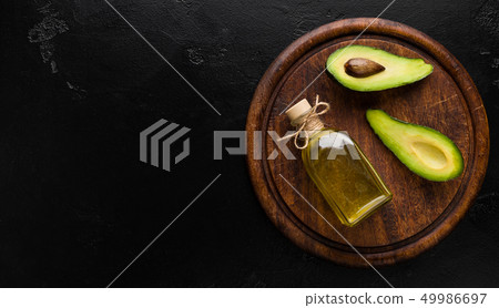 Two avocado halves and bottle of oil on board 49986697