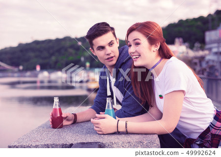 Beautiful happy couple leaning on concrete parapet and having bottles 49992624