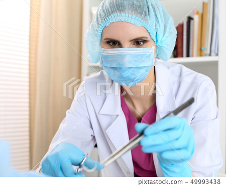 Beautiful female surgeon in mask hold needle, forceps and tweezers Beautiful female surgeon in mask hold needle, forceps and tweezers 49993438