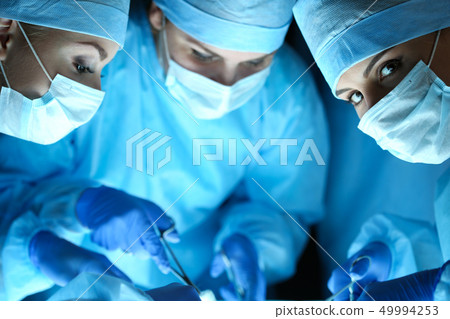 Three surgeons at work operating in surgical theatre Three surgeons at work operating in surgical theatre 49994253