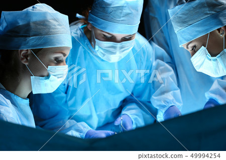 Group of surgeons at work operating in surgical theatre Group of surgeons at work operating in surgical theatre 49994254
