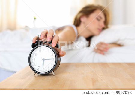 Sleepy young woman trying kill alarm clock Sleepy young woman trying kill alarm clock 49997058