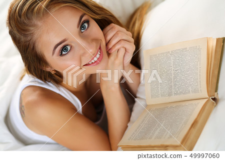 Young beautiful smiling blonde woman lying in bed reading book Young beautiful smiling blonde woman lying in bed reading book 49997060