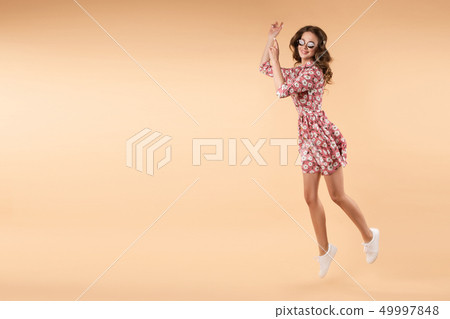 Girl in pink floral dress jumping and laughing in 49997848