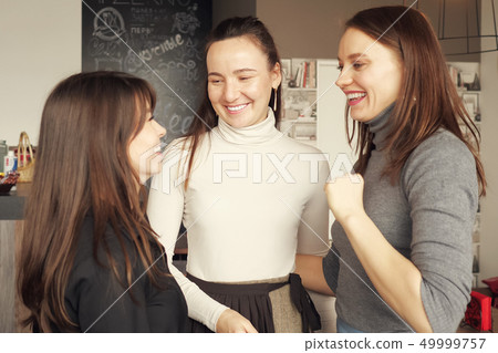 Three women friends are hugging together greeting. Friendly meeting in cafe. 49999757