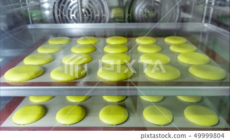 Macaroons on stencil silicone mat is baking in oven. View through the glass. 49999804