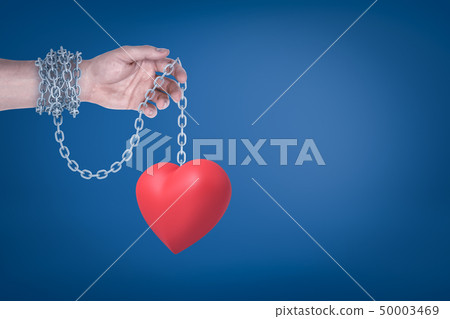 Close-up of man's hand with metal chain around wrist holding red valentine heart hanging on the 50003469