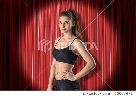 Close-up of young woman in black sport crop top and shorts standing in half-turn with one hand on 50003471