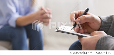 Specialist noting problems of young woman at psychotherapy session 50004149