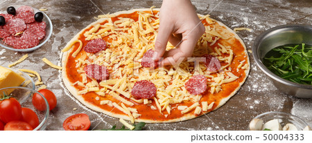 Chef adding salami to italian pizza at kitchen table Chef adding salami to italian pizza at kitchen table 50004333