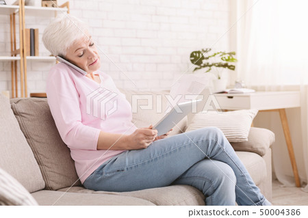 Busy senior woman consulting client on phone and reading contract Busy senior woman consulting client on phone and reading contract 50004386