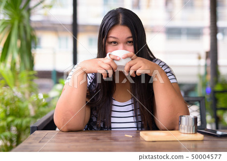 Beautiful overweight Asian woman relaxing at the coffee shop Beautiful overweight Asian woman relaxing at the coffee shop 50004577
