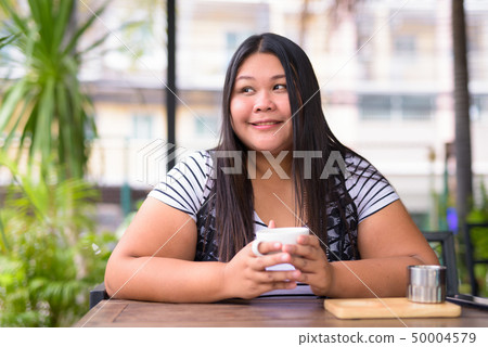 Beautiful overweight Asian woman relaxing at the coffee shop Beautiful overweight Asian woman relaxing at the coffee shop 50004579